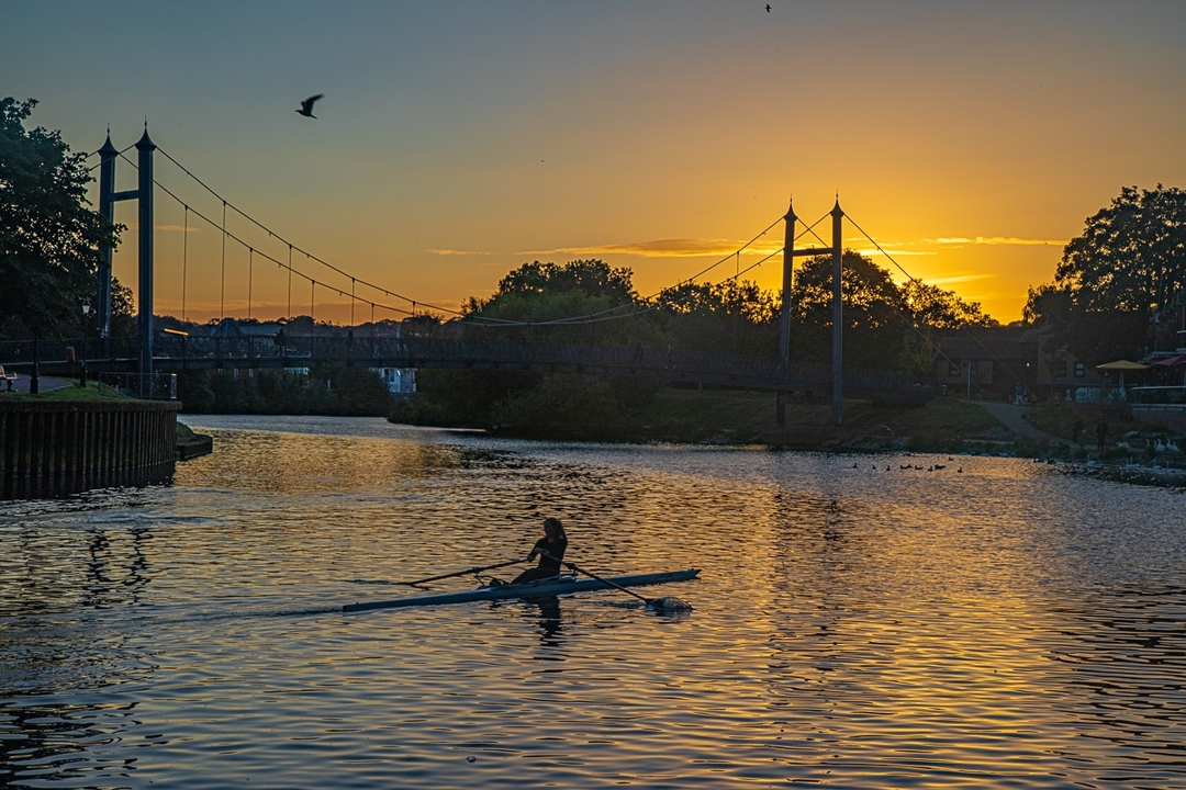Rameur sur une rivière au coucher du soleil avec un pont suspendu en arrière-plan.