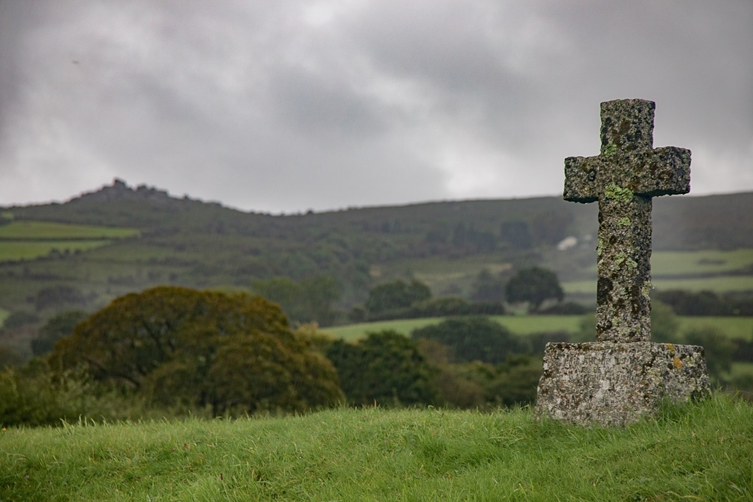 Croix de pierre patinée sur une colline herbeuse.