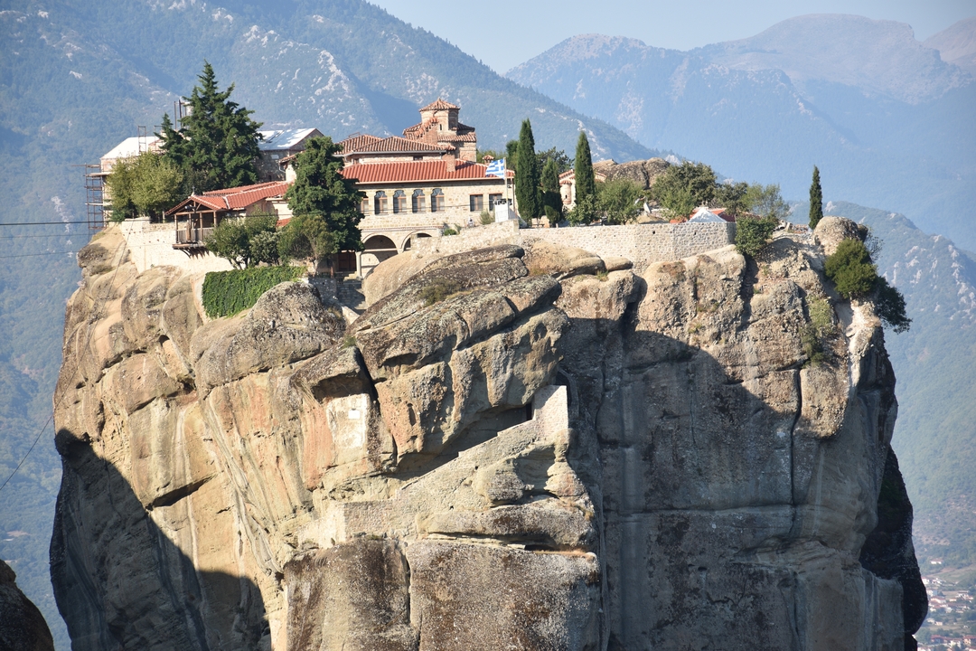 Monastery perched atop a towering stone pillar at Meteora with hazy mountains beyond