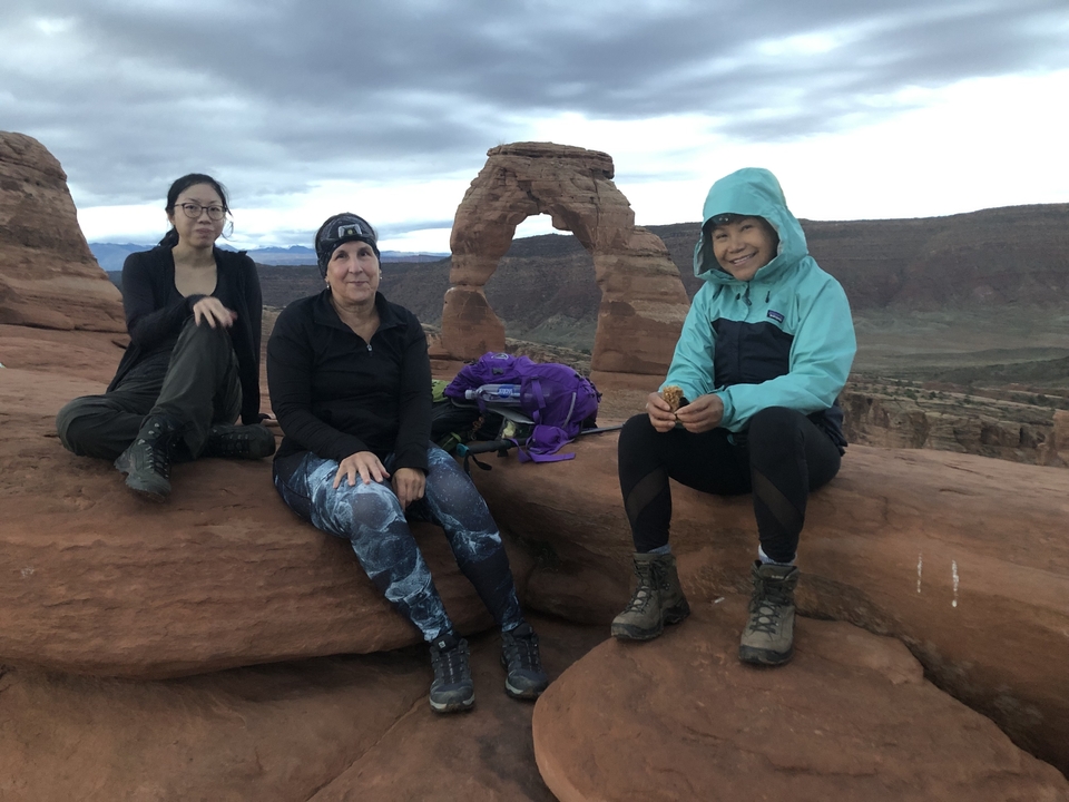 Trois femmes assises sur un rocher devant une arche.