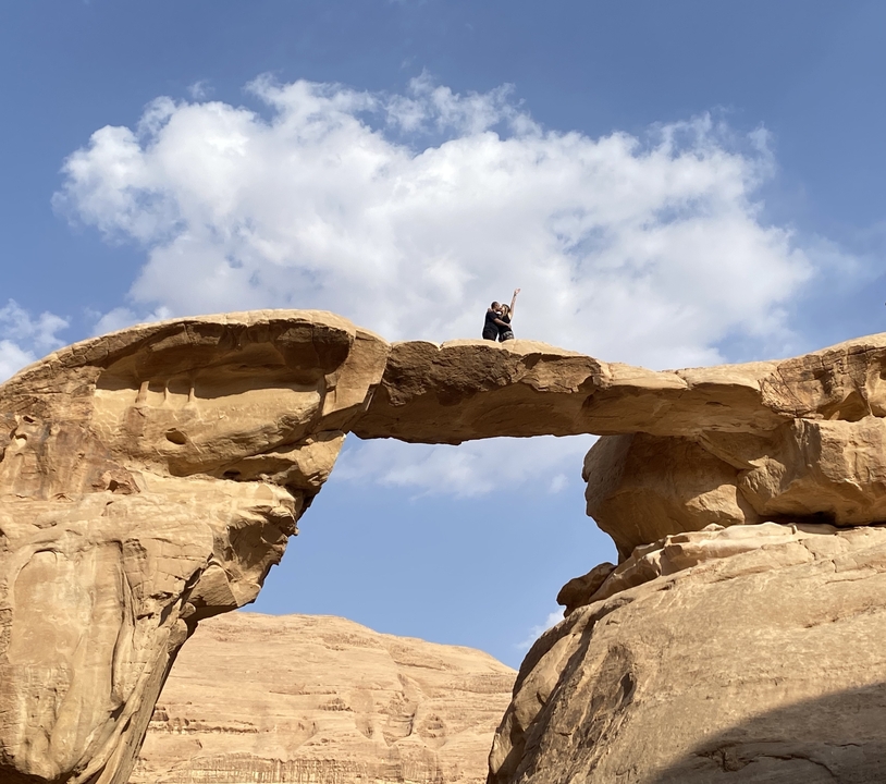 Personne debout sur une arche rocheuse naturelle sous un ciel bleu.