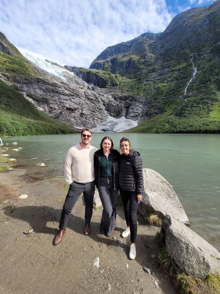 Three people posing near a glacier and lake.