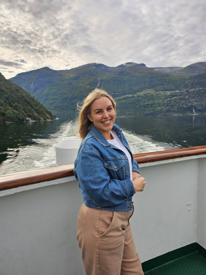 Person leaning on a railing on a boat with views of mountains.