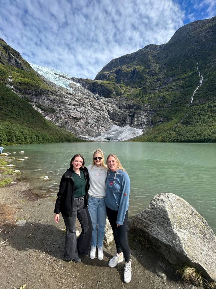 Three people posing by a glacier and lake.