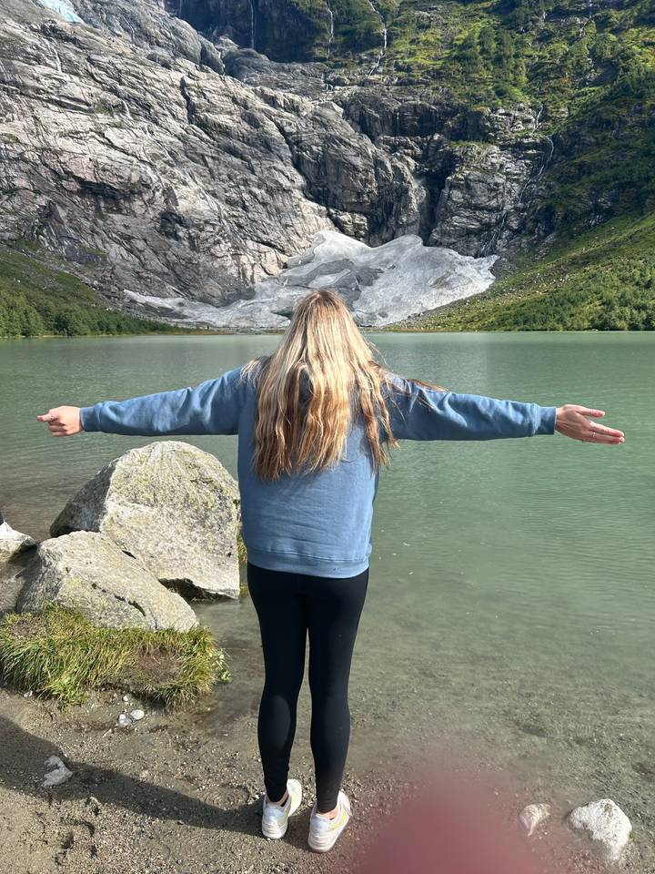 Person standing with arms extended near a glacier.