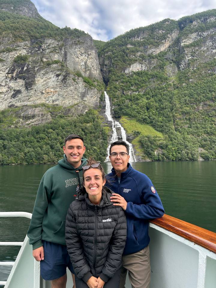 People standing on a boat with a waterfall and rocky cliffs in the background.