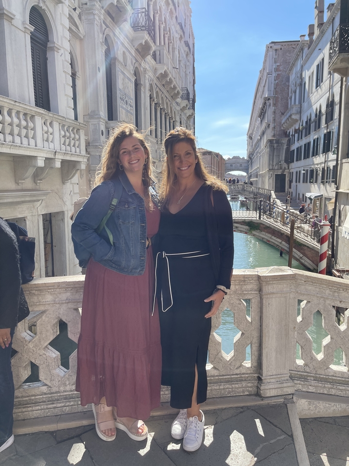 Deux femmes debout sur un pont au-dessus d'un canal avec des bâtiments historiques en arrière-plan.
