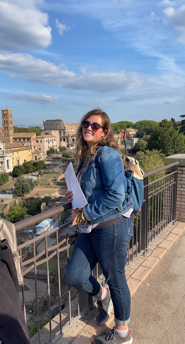 Une personne avec des lunettes de soleil et un sac à dos profitant de la vue d'une ville historique avec des ruines et des arbres.