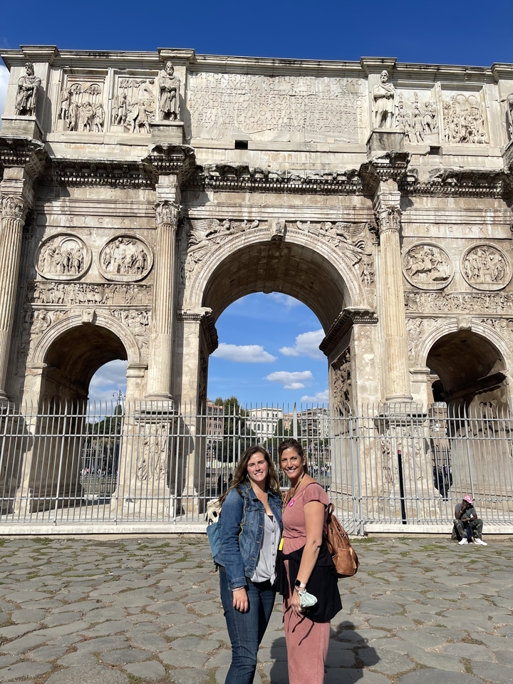 Deux personnes debout devant une grande arche ancienne avec des sculptures détaillées.