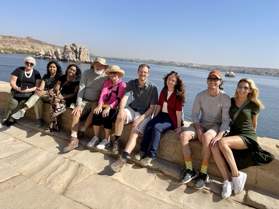 Groupe de voyageurs assis sur un rebord de pierre au bord du Nil avec des îles rocheuses.