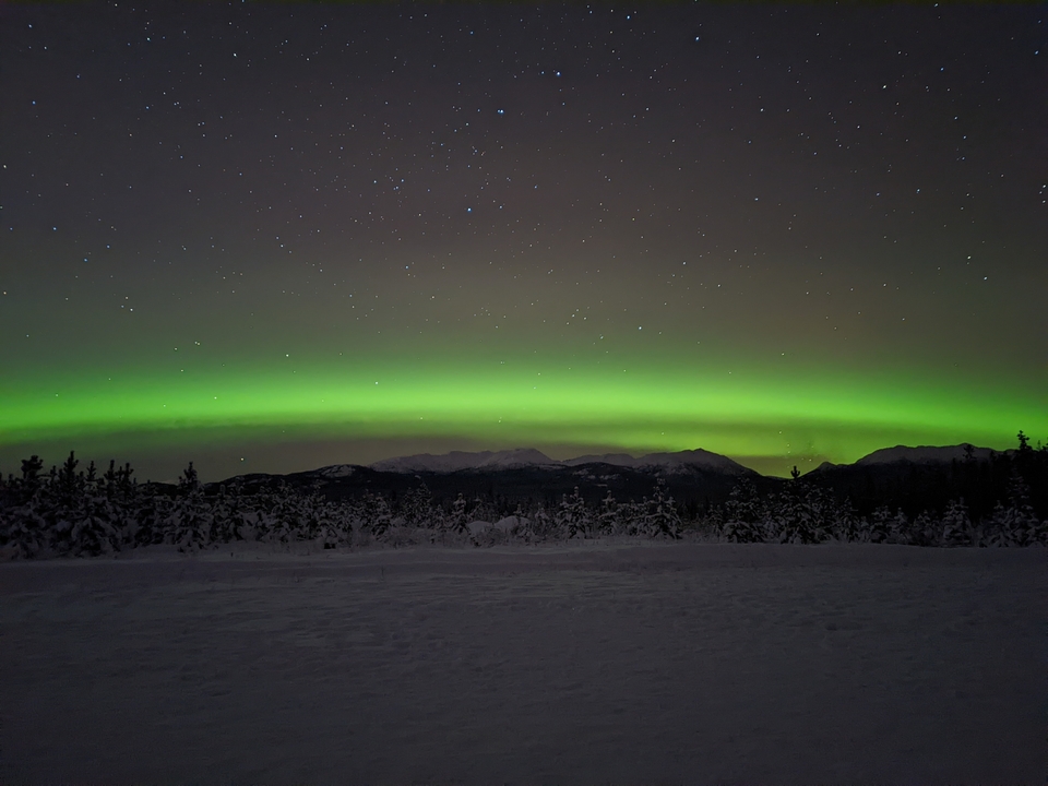 Aurore boréale au-dessus d'un paysage montagneux enneigé la nuit.