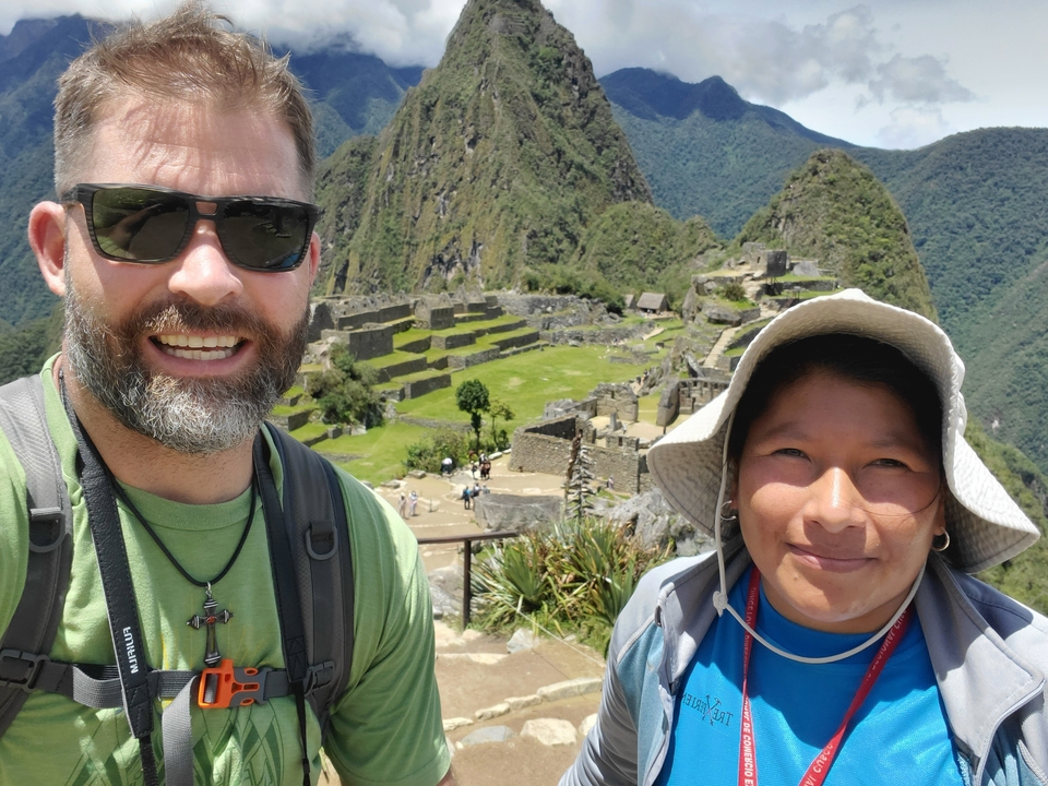 Deux personnes souriantes avec les ruines du Machu Picchu en arrière-plan.