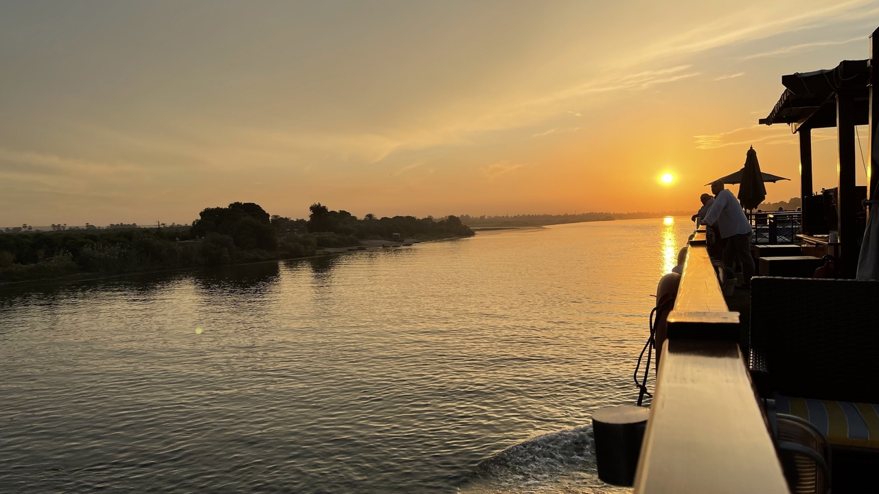 Des touristes sur une terrasse, profitant du coucher de soleil au-dessus d'une rivière.