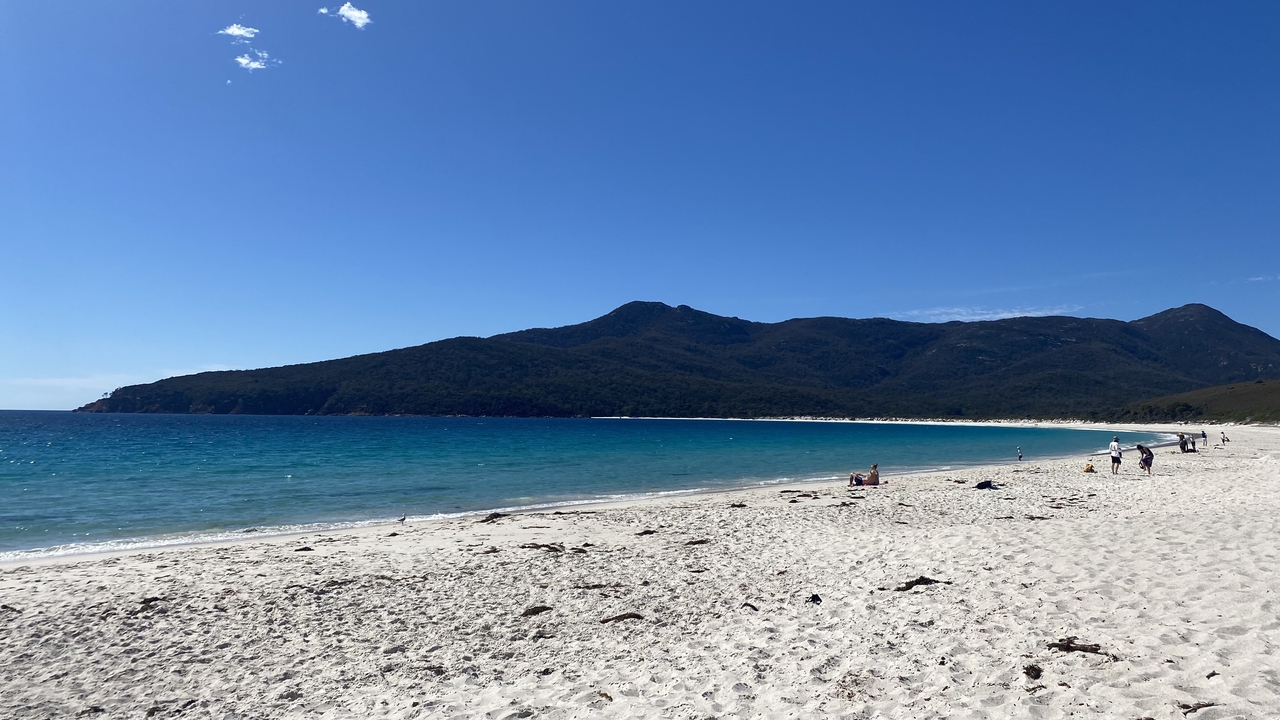 Plage de sable blanc avec des eaux turquoise et des collines au loin.