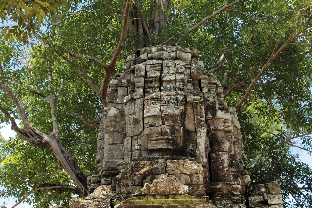 Structure de pierre ancienne avec un visage sculpté entourée d'arbres.