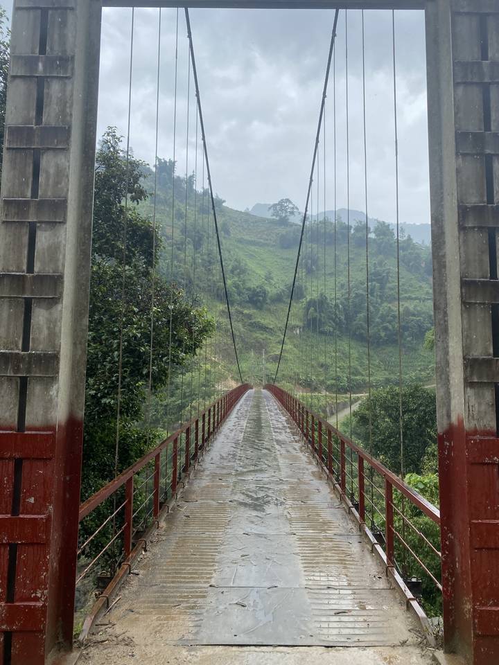 Un étroit pont suspendu au-dessus d'une rivière dans un environnement brumeux.