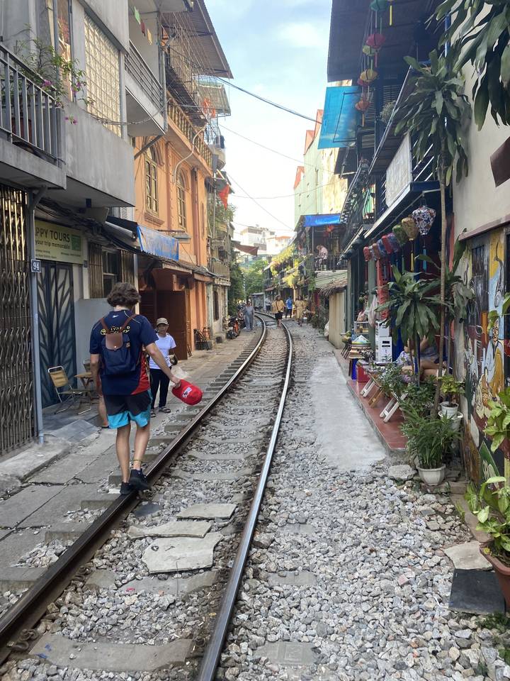 Des gens qui marchent le long d'une rue étroite avec des voies ferrées.