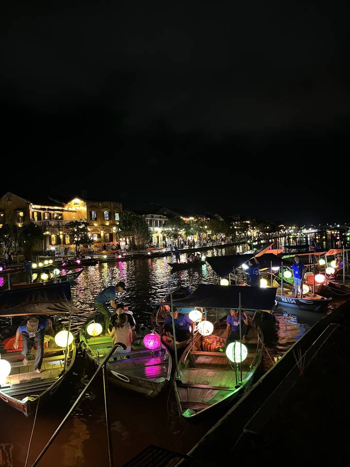 Scène nocturne d'une rivière bordée de bateaux colorés éclairés par des lanternes.
