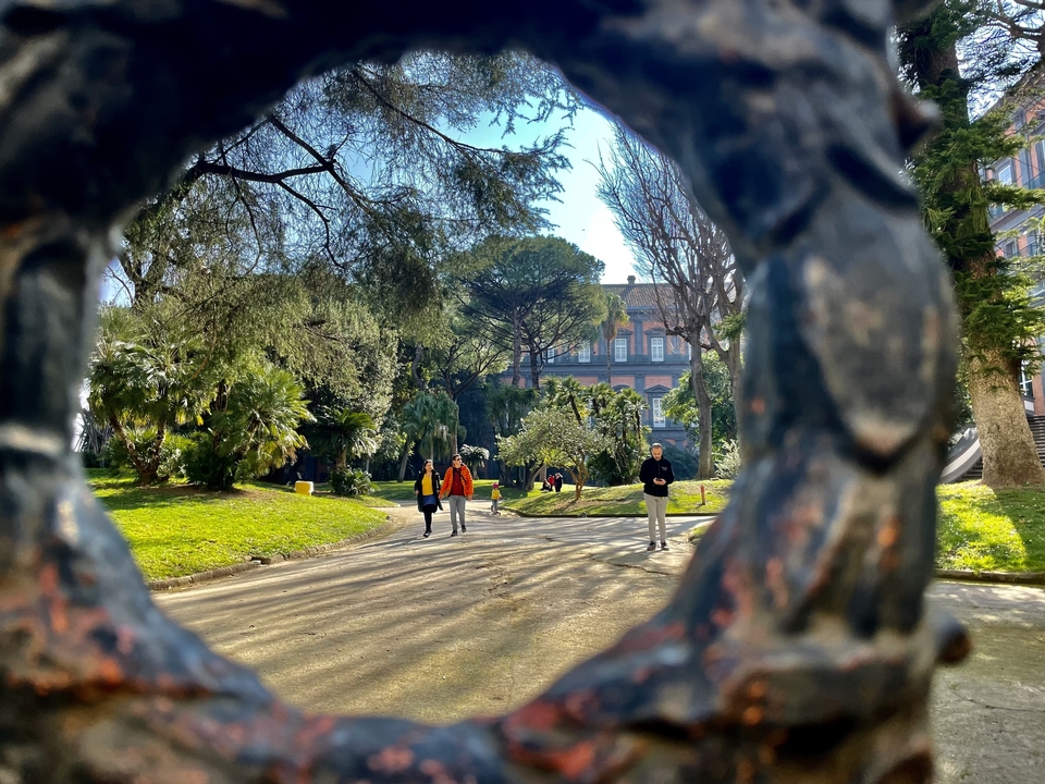 Des personnes se promènent dans un parc avec une végétation luxuriante et un bâtiment historique.