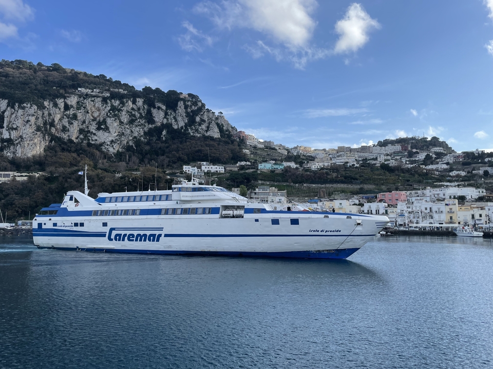 Un grand ferry nommé 'Caremar' près d'une jetée avec des collines en arrière-plan.