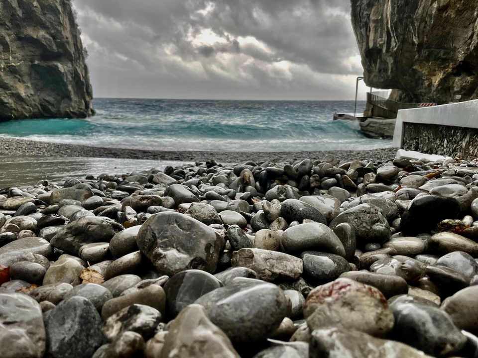 Plage rocheuse avec des vagues qui se brisent sous un ciel couvert.