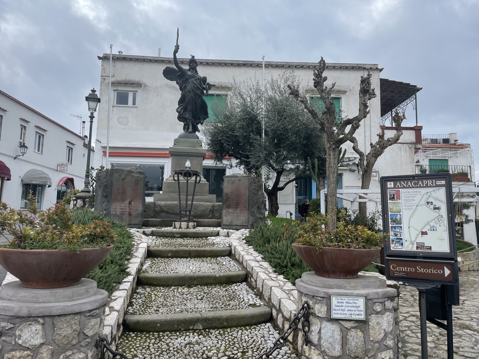 Une statue sur une place avec une carte montrant 'Anacapri' et diverses plantes.