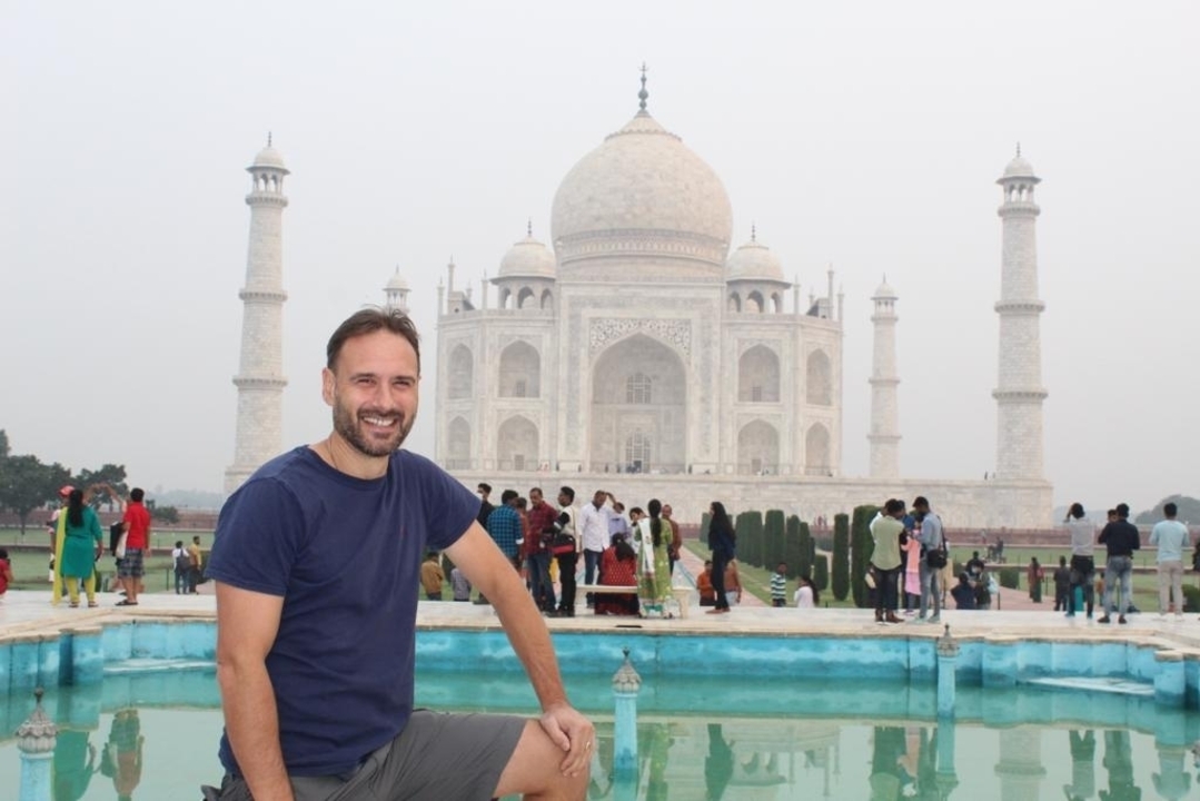Un homme près d'une piscine avec le Taj Mahal en arrière-plan.