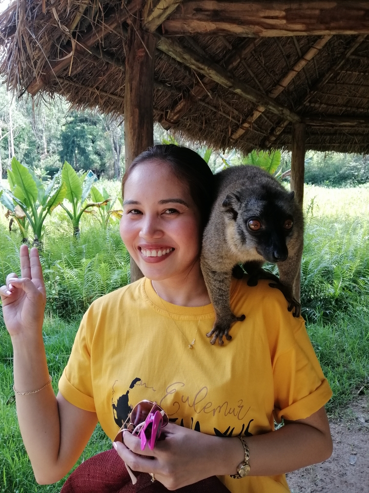 Femme souriante avec un lémurien sur l'épaule.