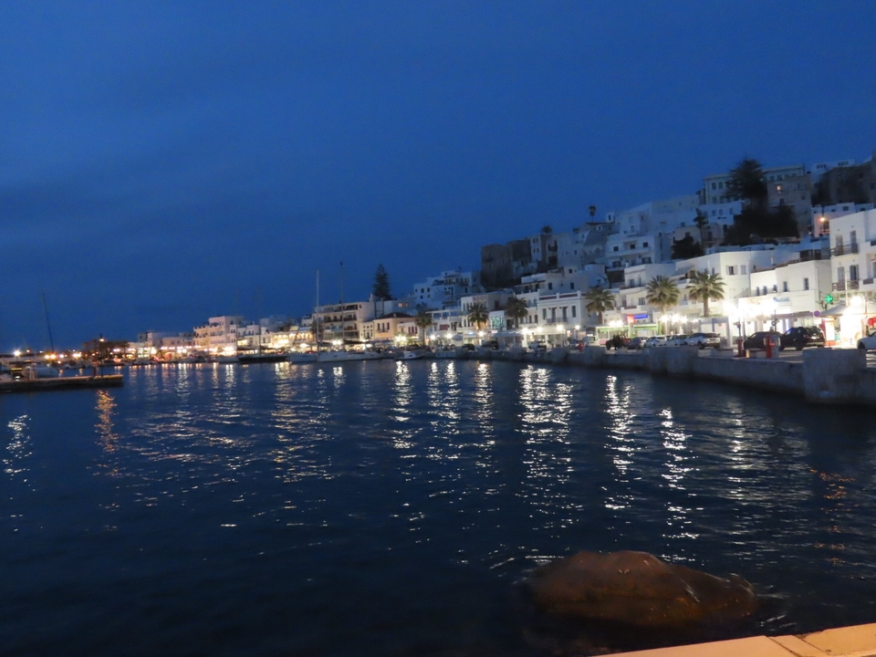 Vue nocturne d'une ville côtière avec les lumières se reflétant sur l'eau.