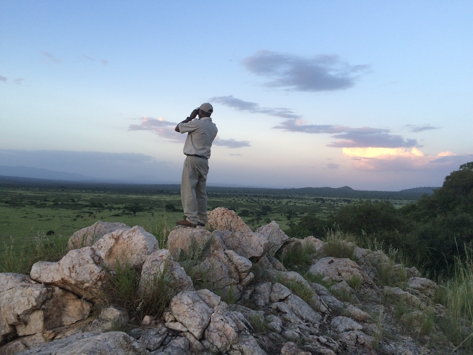 Une personne debout sur des rochers, regardant à travers des jumelles un vaste paysage.