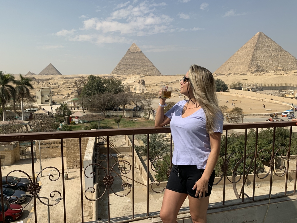 Personne profitant d'une vue sur les pyramides avec une boisson.