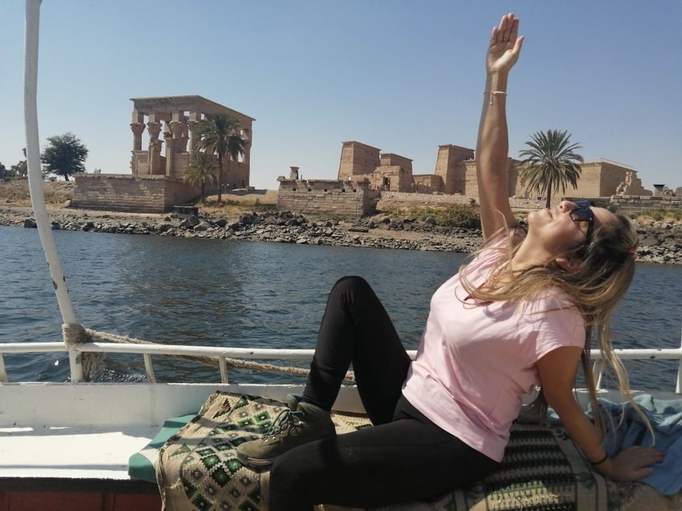 Femme sur un bateau avec des ruines antiques en arrière-plan.