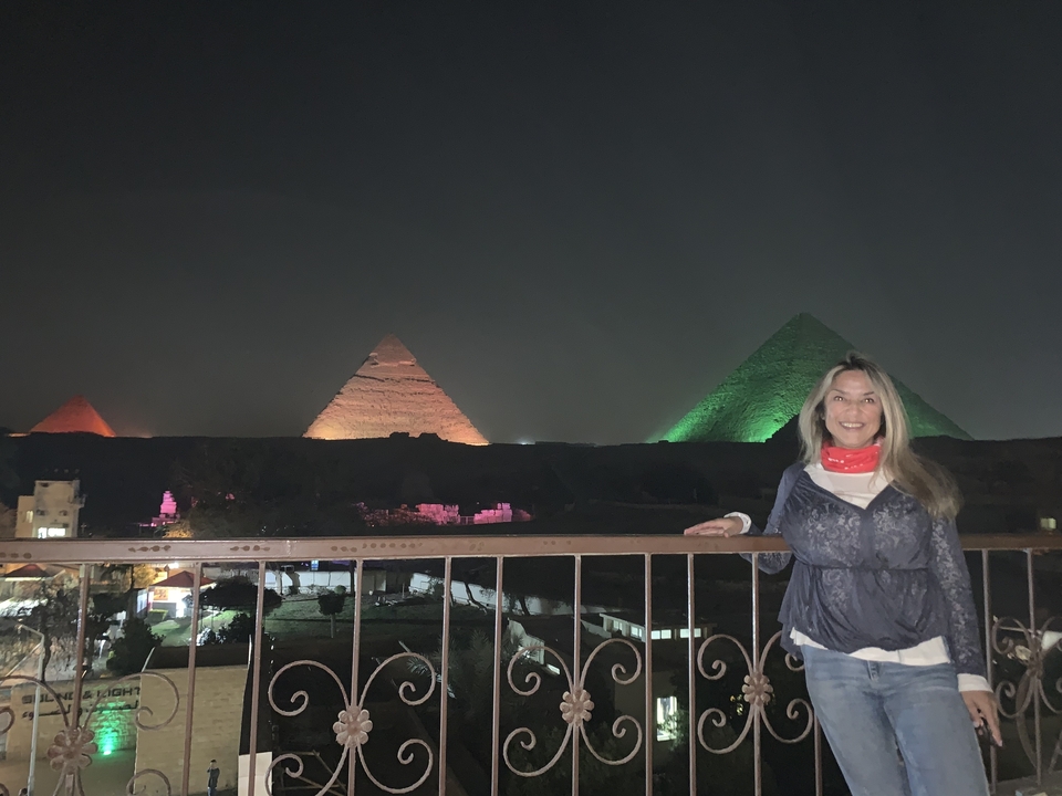Personne posée devant des pyramides illuminées la nuit.