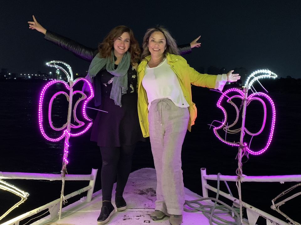 Deux femmes posant sur un bateau avec des décorations néon la nuit.