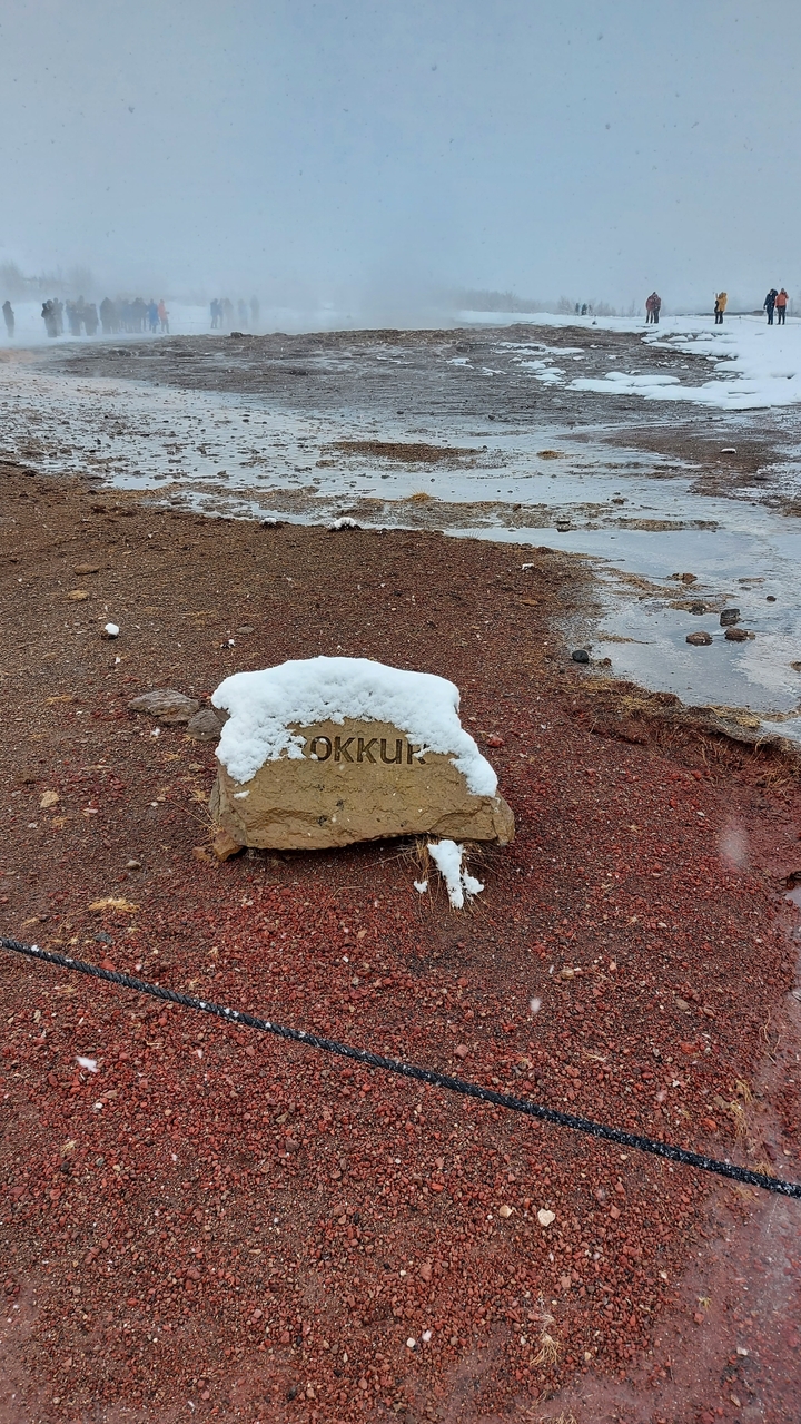 Rocher avec texte et neige, au milieu d'un paysage volcanique et aride.