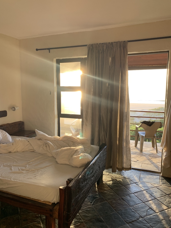 Une vue de chambre avec des rideaux ouverts montrant le lever du soleil sur la plage.