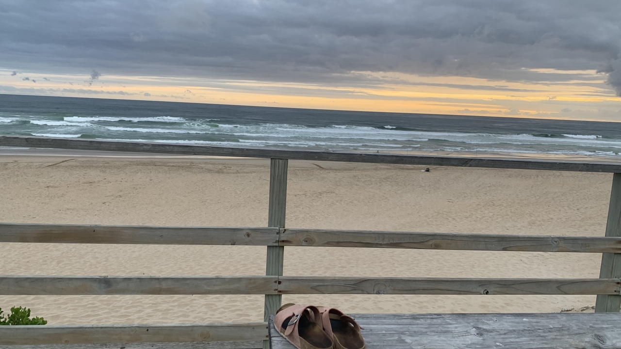 Vue sur la plage avec coucher de soleil et une paire de sandales sur une rambarde.