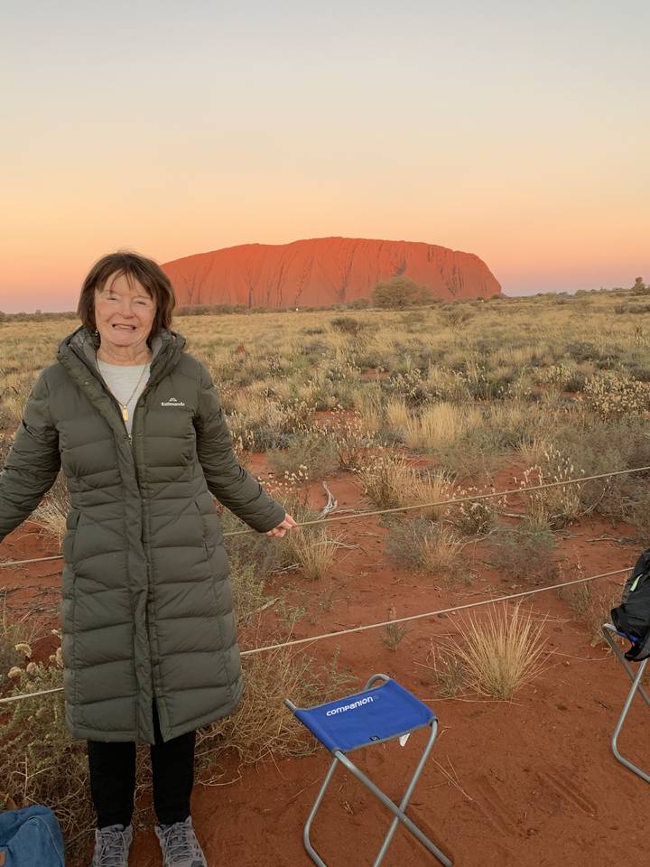 Persona sonriendo frente a un paisaje desértico y montañoso durante la puesta de sol.