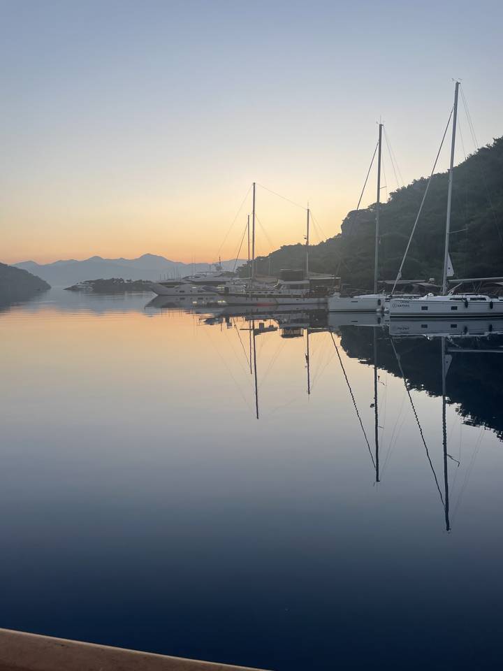 Bateaux et mâts dans un port face à un coucher ou lever de soleil.