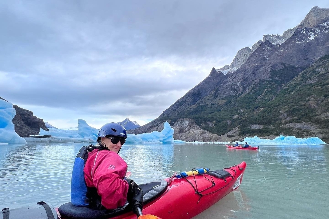 Kayaker in red dry-suit paddling among blue icebergs on a calm glacial lake backed by steep mountains