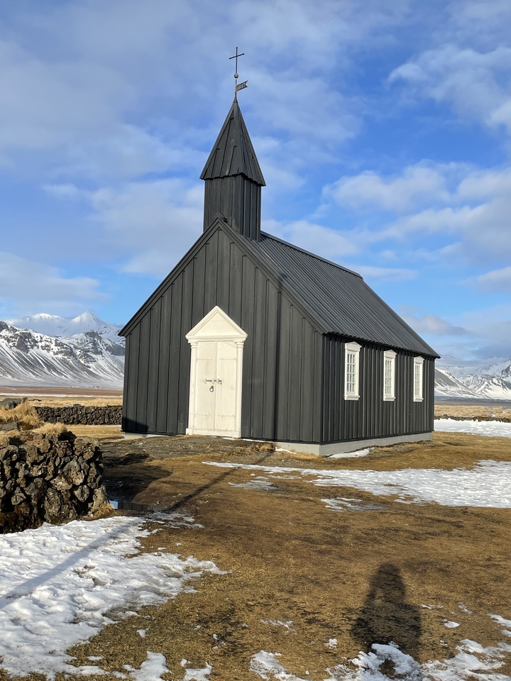 Une petite église noire dans un paysage enneigé.