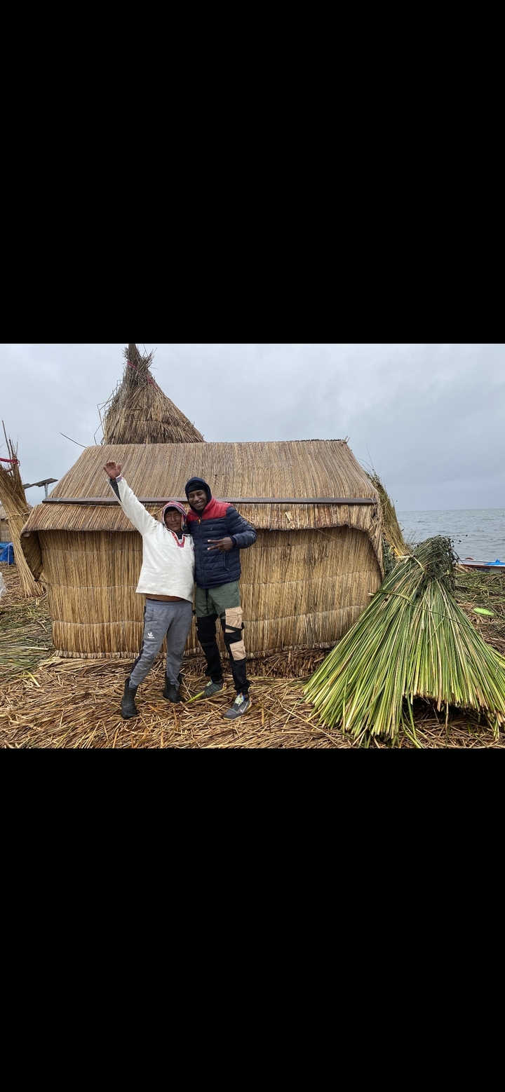 Deux personnes posant devant une maison traditionnelle en roseaux au bord d'un lac.