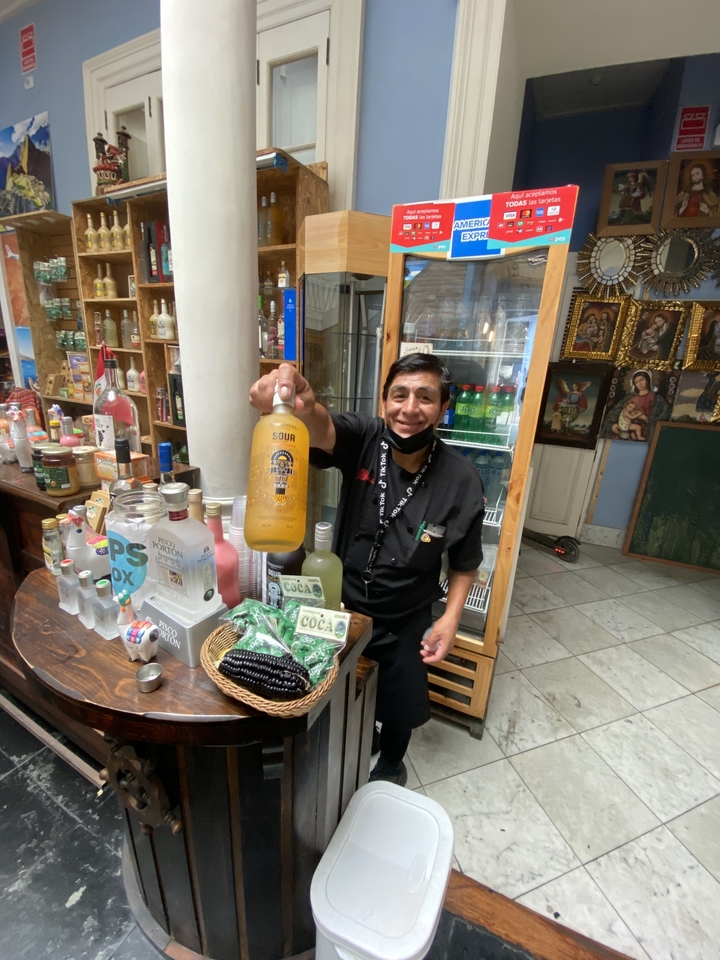 Homme présentant une bouteille étiquetée 'Sour Chili' dans une petite boutique.