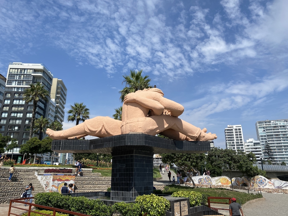 Statue publique d'un couple qui s'enlace dans un parc avec un paysage urbain en arrière-plan.