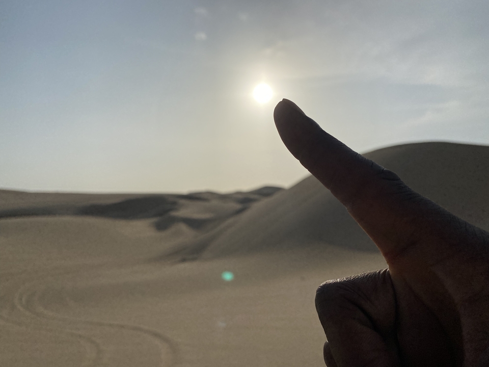 Doigt pointé vers le soleil au-dessus des dunes de sable.