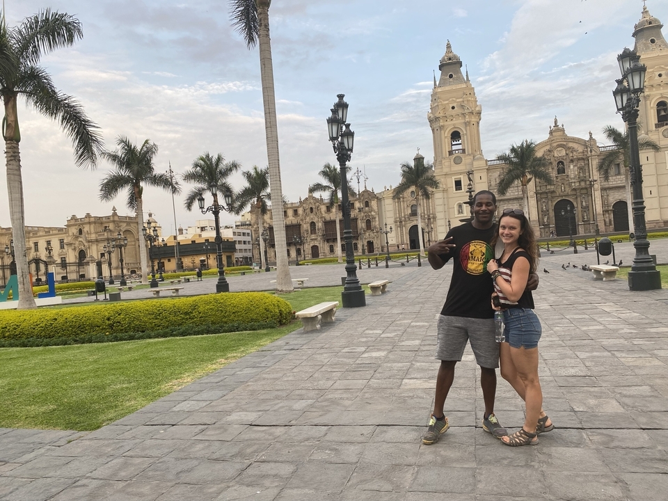 Deux personnes posant devant des bâtiments coloniaux sur la place centrale de Lima.