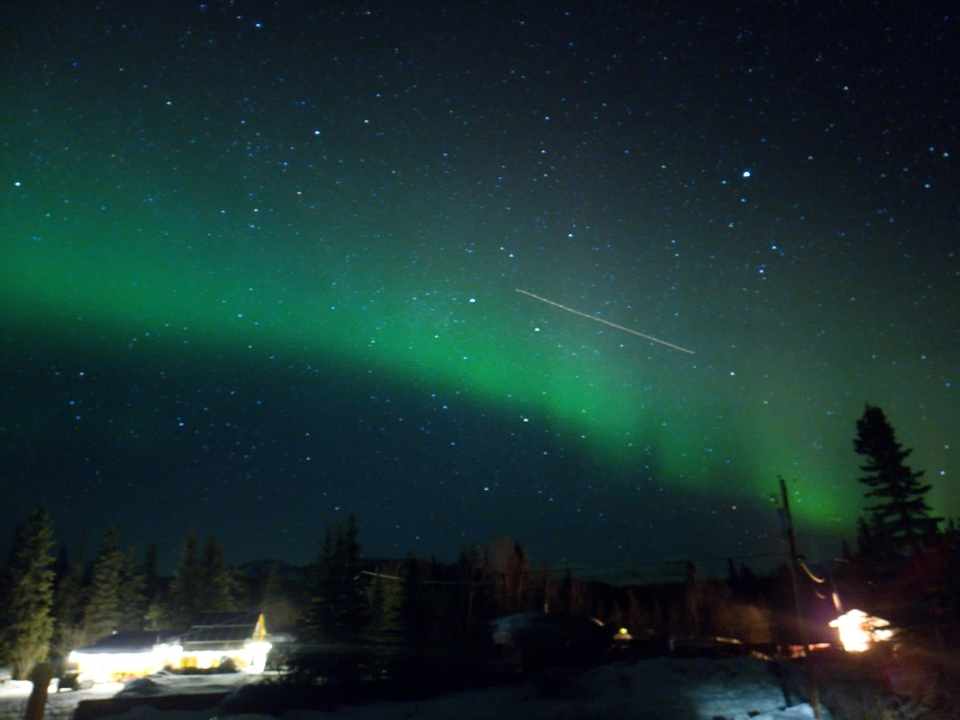 Aurores boréales avec une traînée dans le ciel nocturne au-dessus d'un paysage en silhouette.