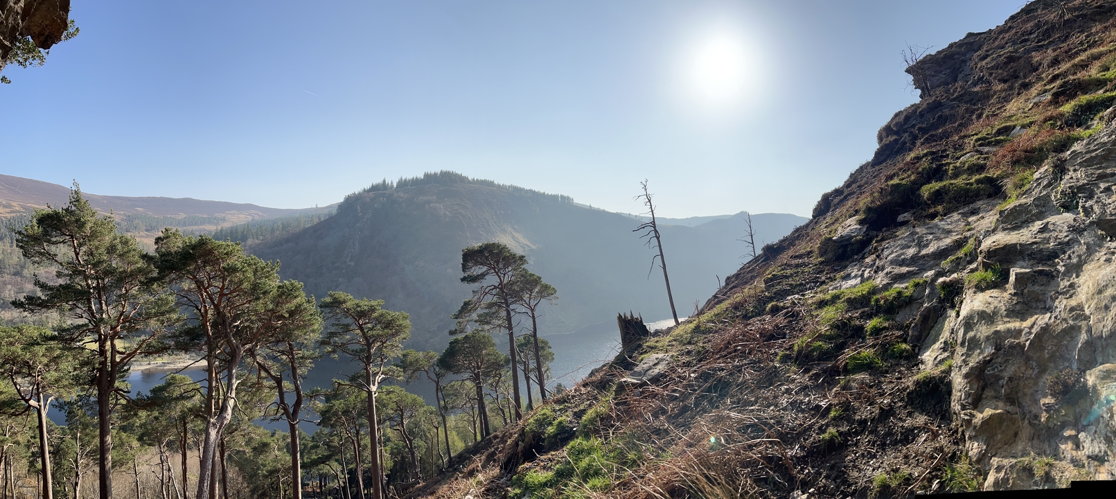 Vue d'un paysage montagneux avec des arbres et un lac au loin.