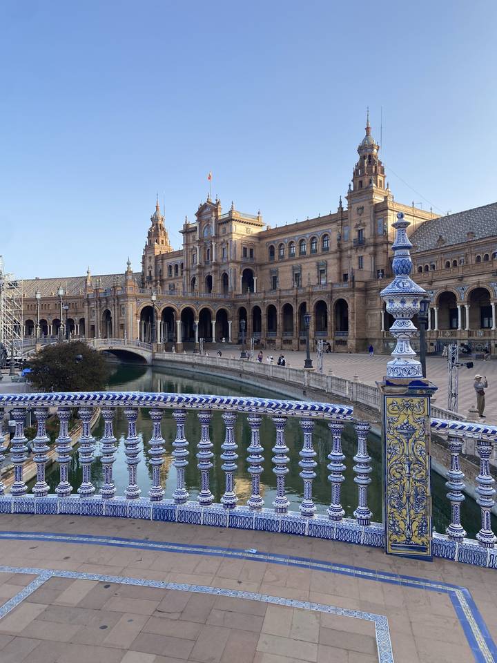 Une vue de la Plaza de España à Séville avec un pont orné et son reflet dans l'eau.