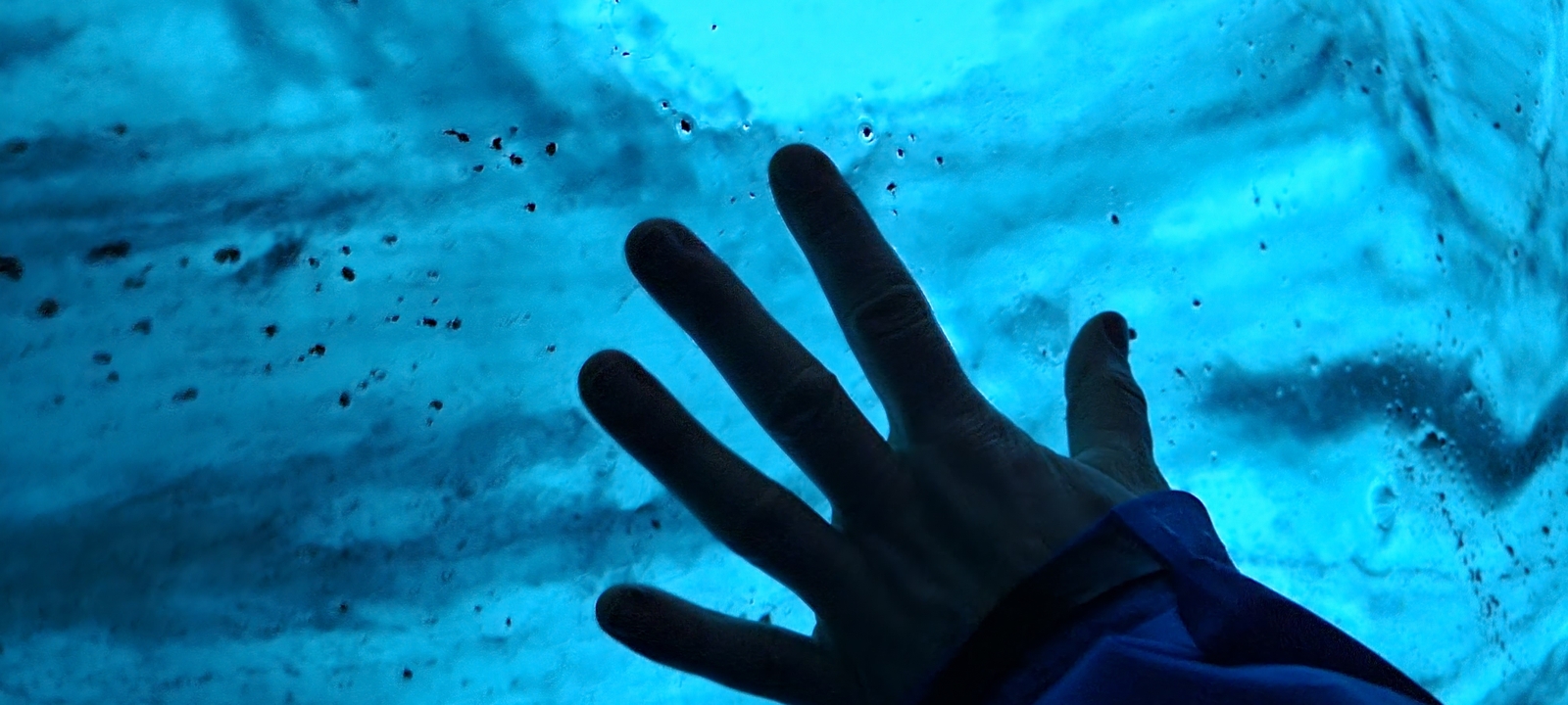 Une personne touchant une surface bleu glacé, probablement un glacier.